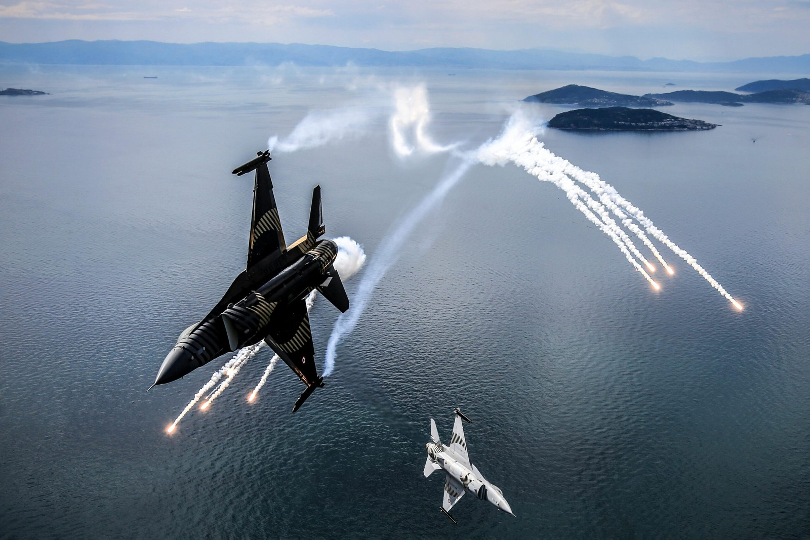 Two fighter jets performing an aerial maneuver over the sea in Türkiye.