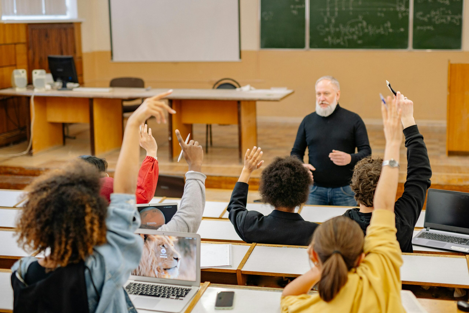 Students actively participate in a university lecture, raising hands and discussing topics.